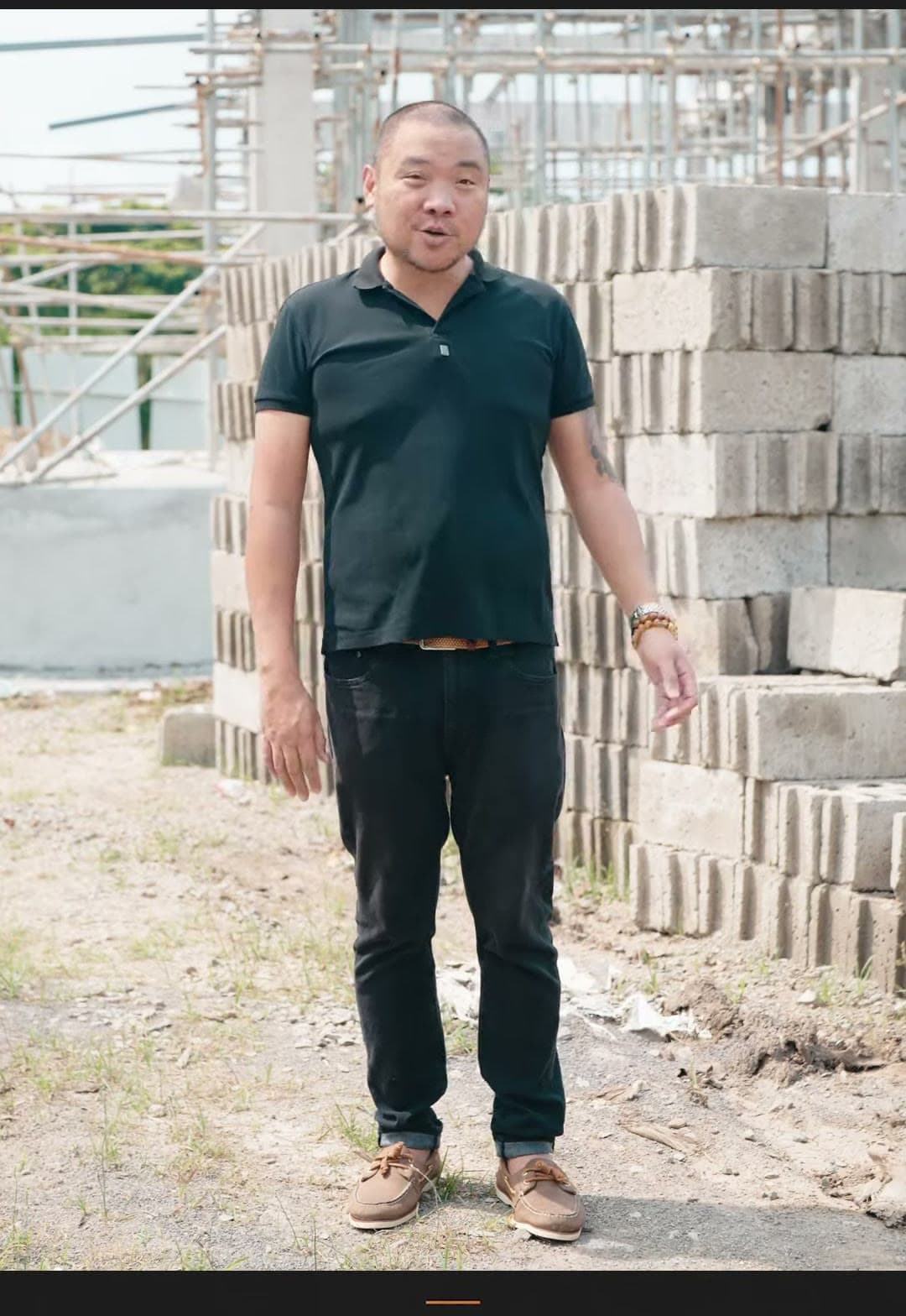 Kuya Erick standing on a construction site beside stacked hollow blocks