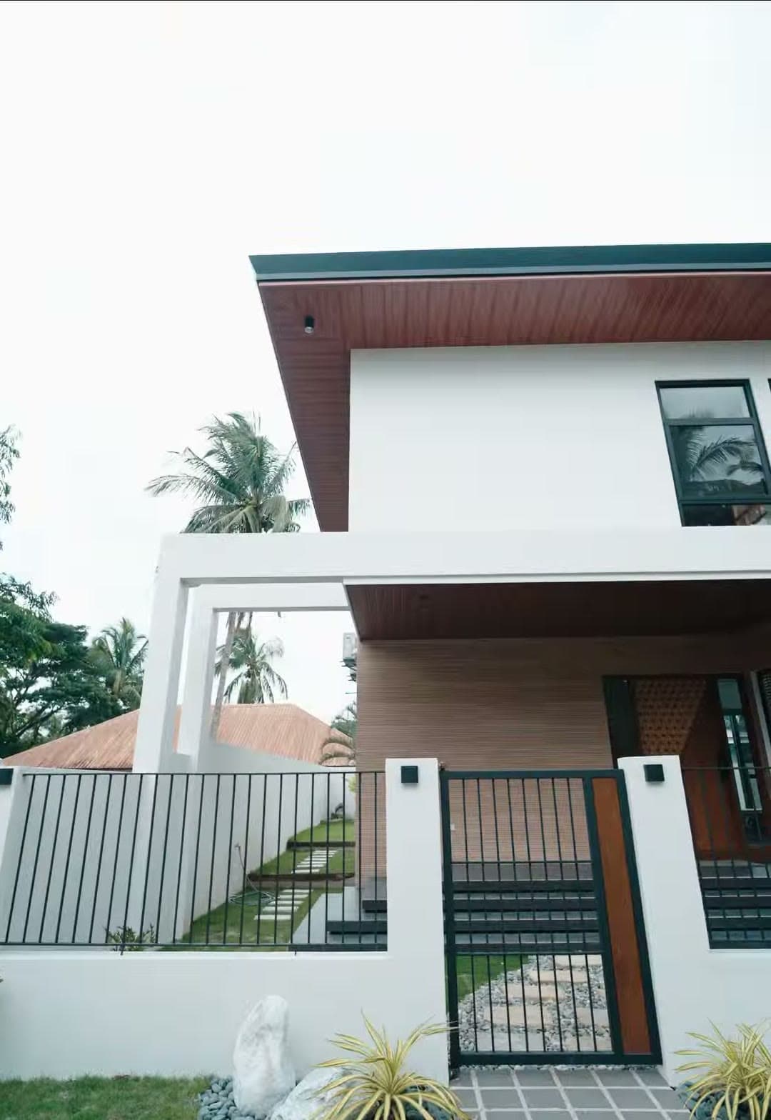 Completed Keystone home: white modern tropical house with a deep wood-lined overhang and palm trees